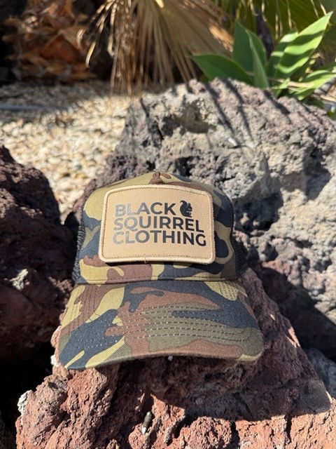Thumbnail: Camo coloured trucker cap with a black squirrel logo on the front
