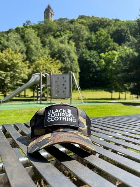 Thumbnail: Camo trucker cap with white black squirrel logo on the front