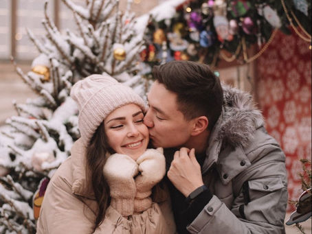 Couple souriant en manteaux d’hiver au marché de Noël, échangeant un moment tendre devant un sapin enneigé