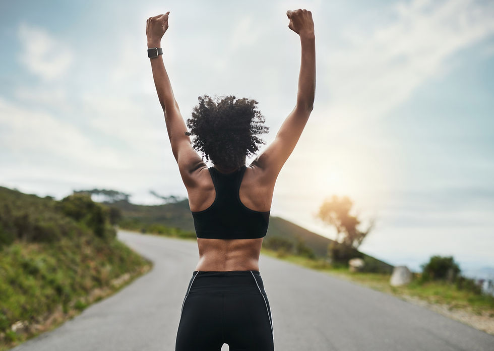 Person in workout gear raises arms in triumph on a scenic road, surrounded by nature. The sky is bright and clear, exuding a victorious mood.