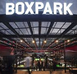 "Entrance to Boxpark Croydon illuminated at dusk, showcasing a vibrant atmosphere with people enjoying food, drinks, and social activities under the large 'BOXPARK' sign."