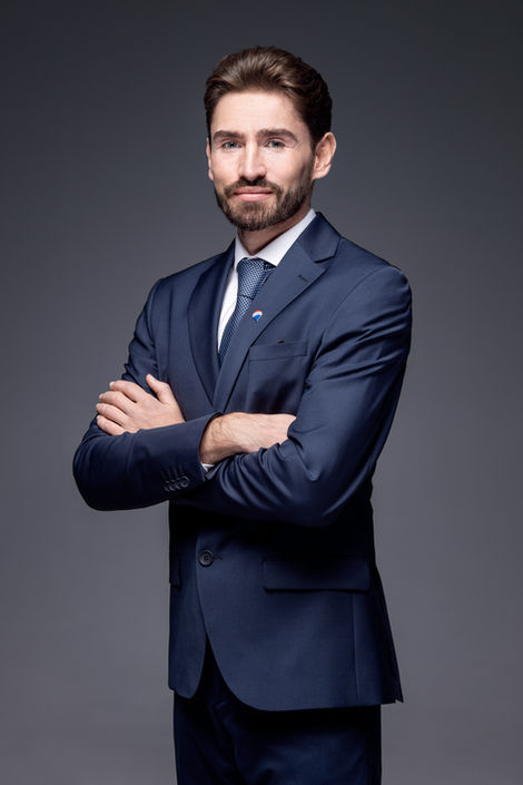 Mann im dunkelblauen Anzug mit verschränkten Armen vor grauem Studiohintergrund