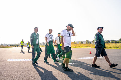 Gruppe Mitarbeitender in Arbeitskleidung läuft über Asphaltfläche bei Sonnenschein