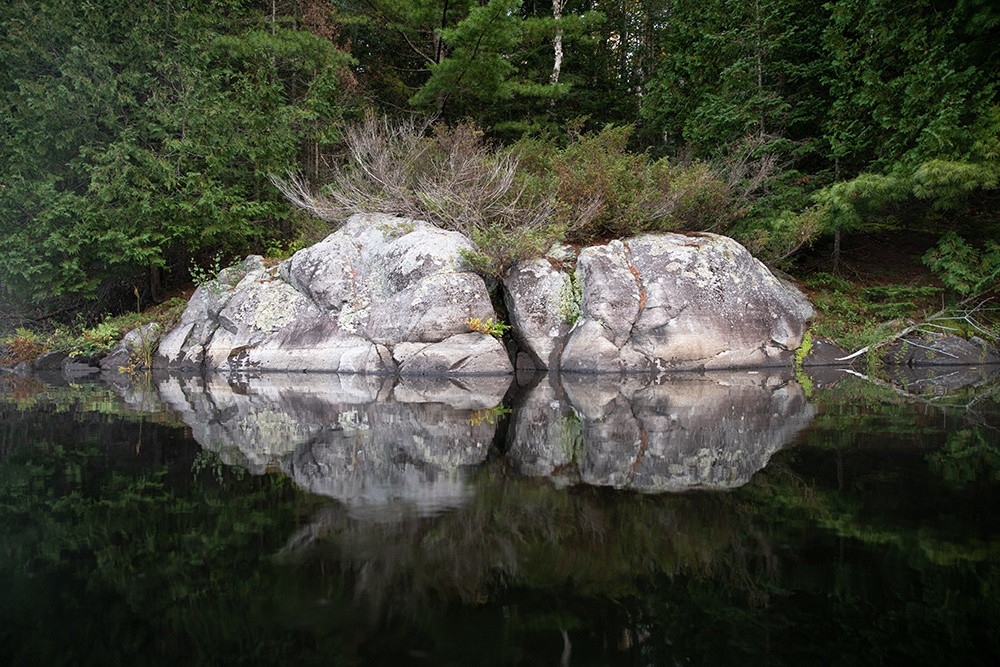 A rock face reflecting on a lake in the early morning.