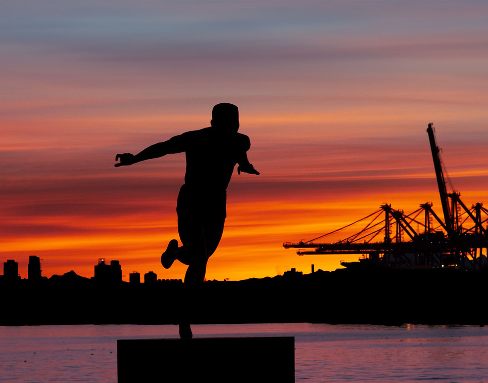 Silhouette-of-a-person-balancing-on-one-foot-against-a-vibrant-orange-sunset-with-city-bui