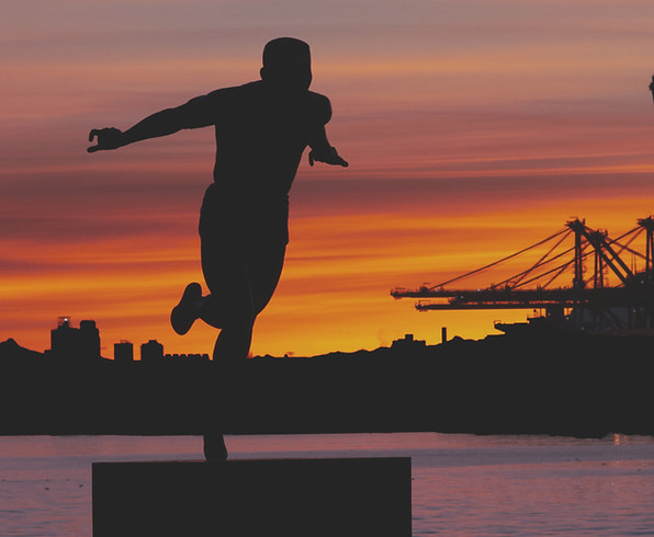 Silhouette of a person balancing on one foot against a vibrant orange sunset, with city bu