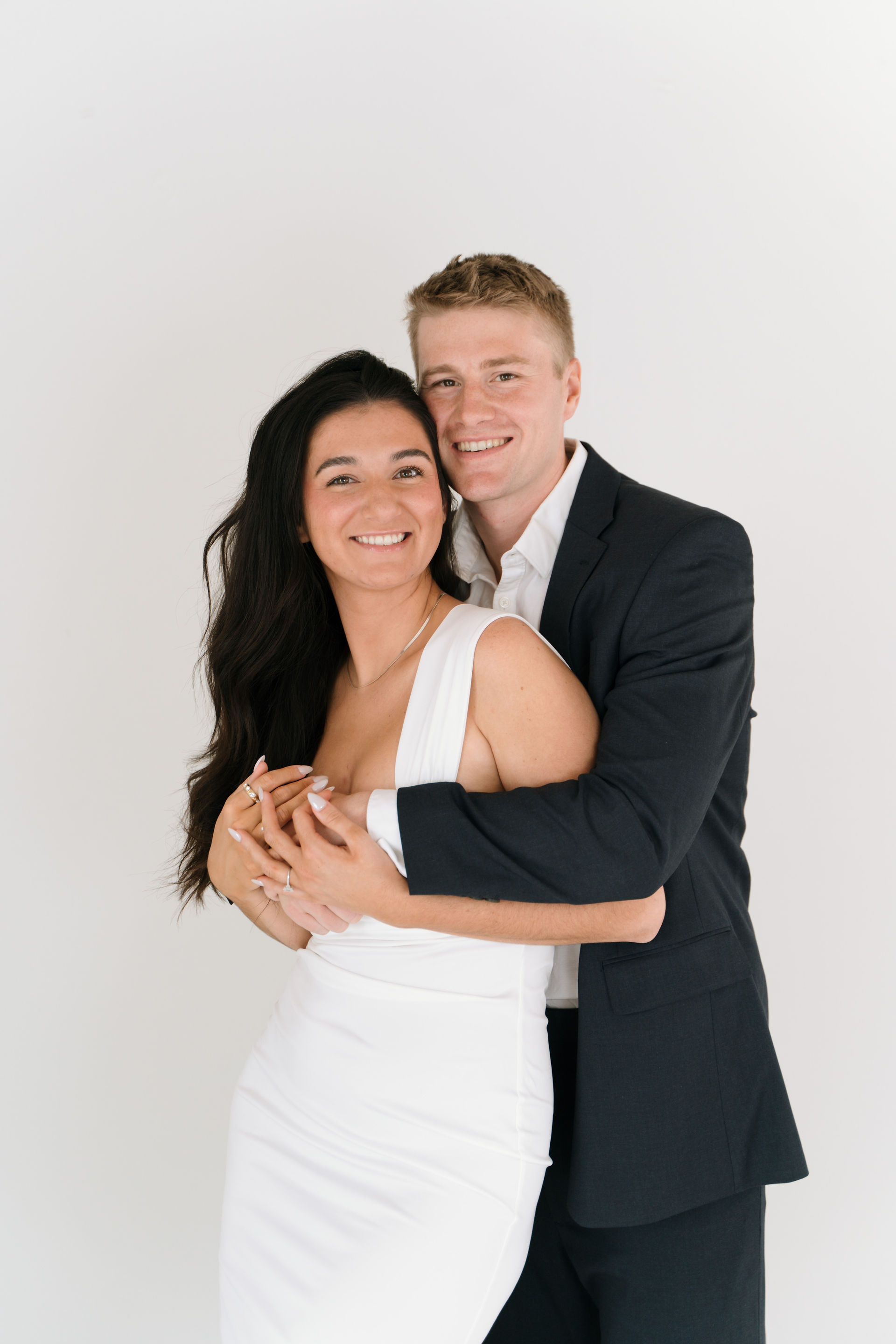 engaged couple pose for camera in front of white back drop
