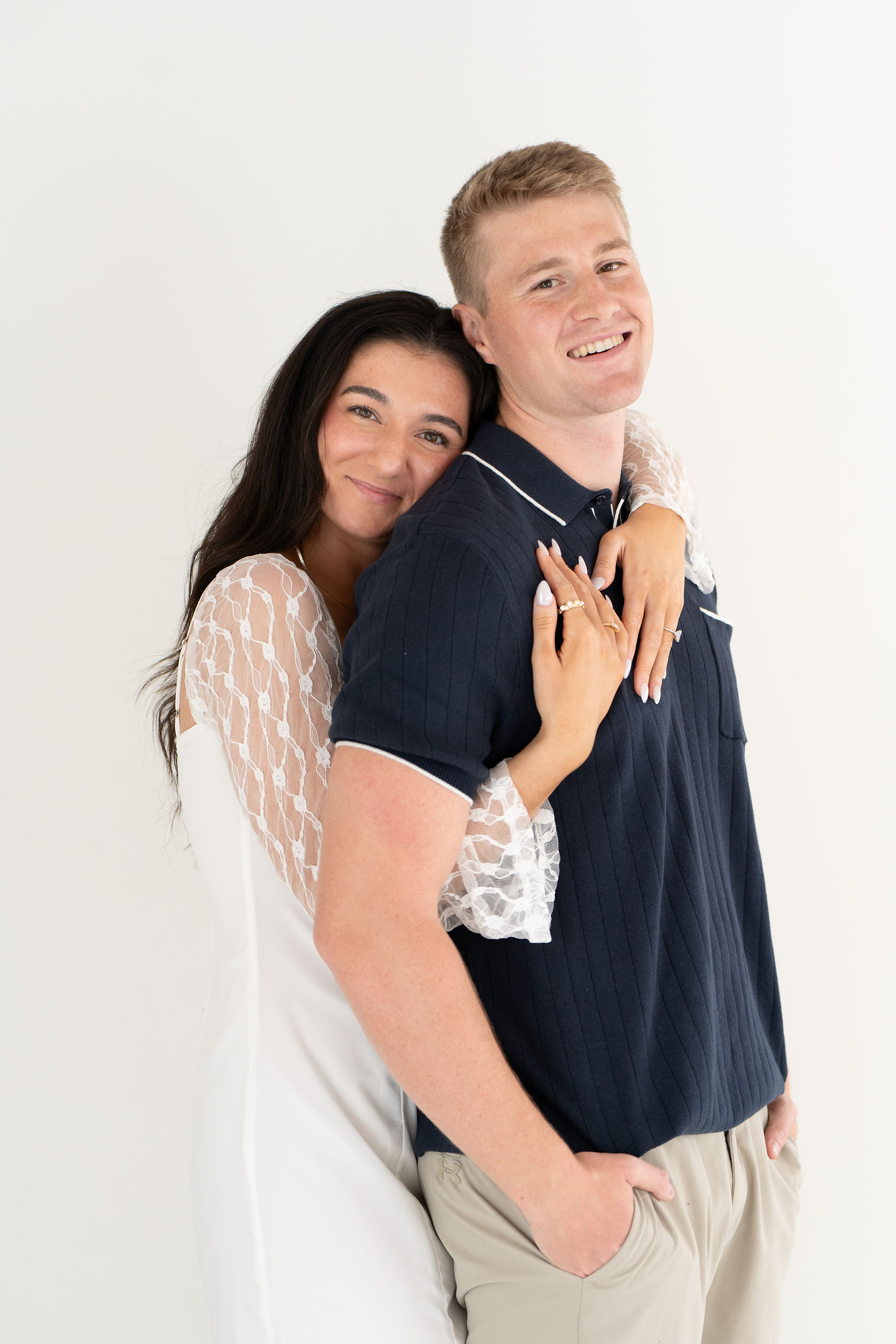 engaged couple pose for camera in front of white back drop