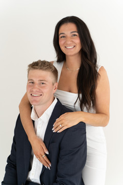 engaged couple pose for camera in front of white back drop