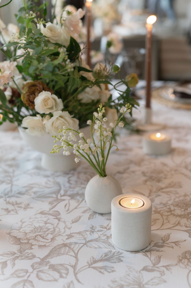 Elegant table setting with floral centerpiece, candles, and silverware on a patterned tablecloth. Chandeliers hang in the upscale venue.