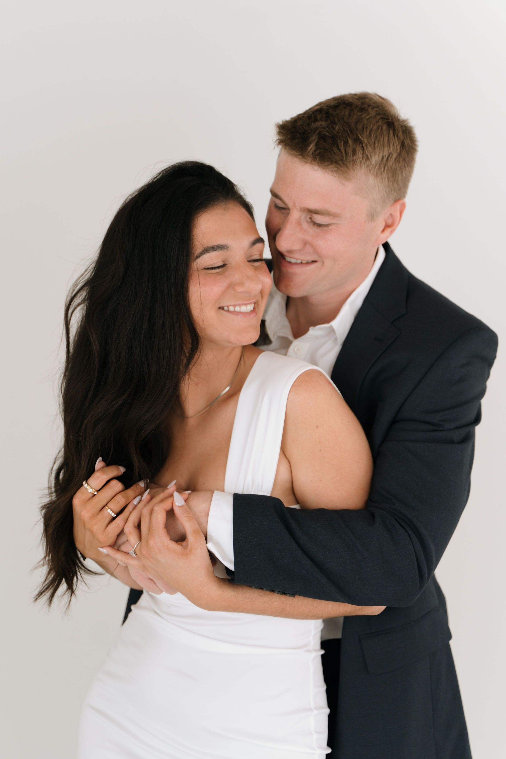 engaged couple pose for camera in front of white back drop