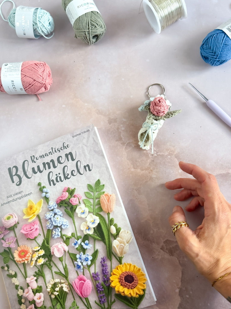 Buch Romantische Blumen häkeln, eine Hand die nach dem gehäkelten Blumenstrauss Schlüsselanhänger greift.