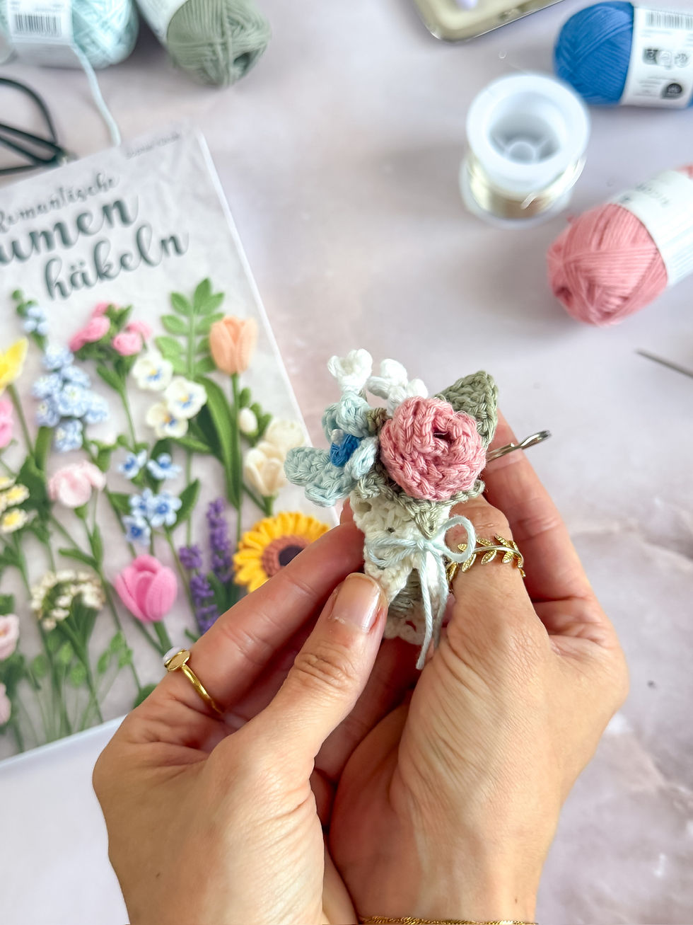 Gehäkelter Blumenanhänger und im Hintergrund das Buch Romanische Blumen häkeln und Häkelmaterial wie Garn und Draht