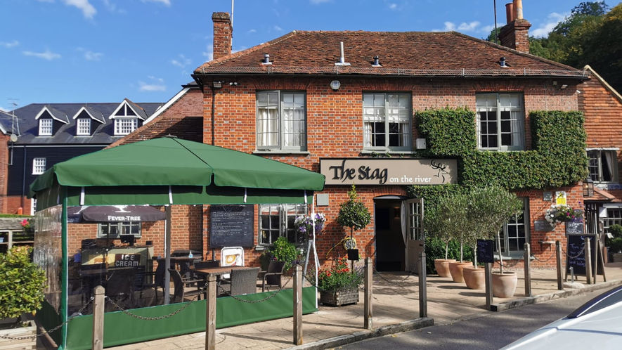 A forest green jumbo umbrella with valance and side sheet in front of country pub.