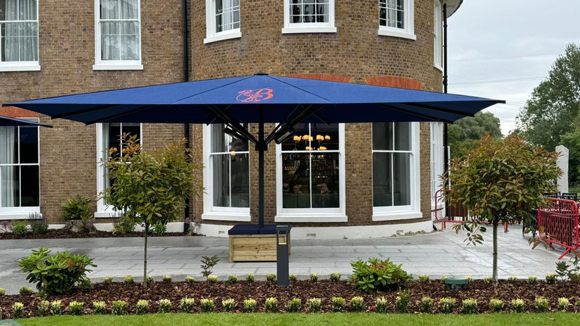A premium golf club terrace with one jumbo umbrellas with an orange logo, freestanding base with seat box.