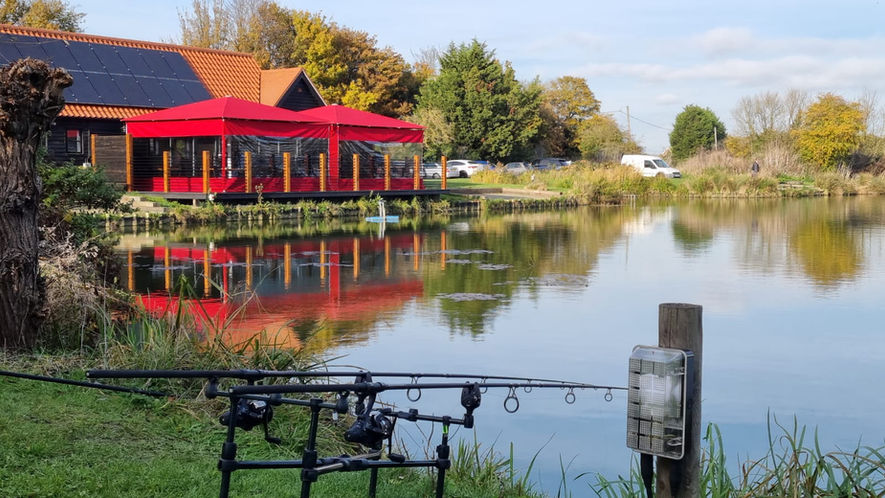 A golf clubhouse terrace by a lake with two red jumbo umbrellas with side sheets to make a large gazebo event space.
