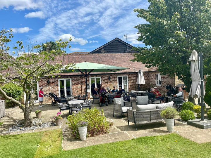 A golf club terrace with grey rope outdoor furniture and a green jumbo umbrella.
