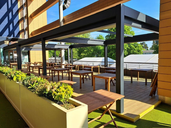 A restaurant decking with an aluminium retractable roof system with roof and sides open.