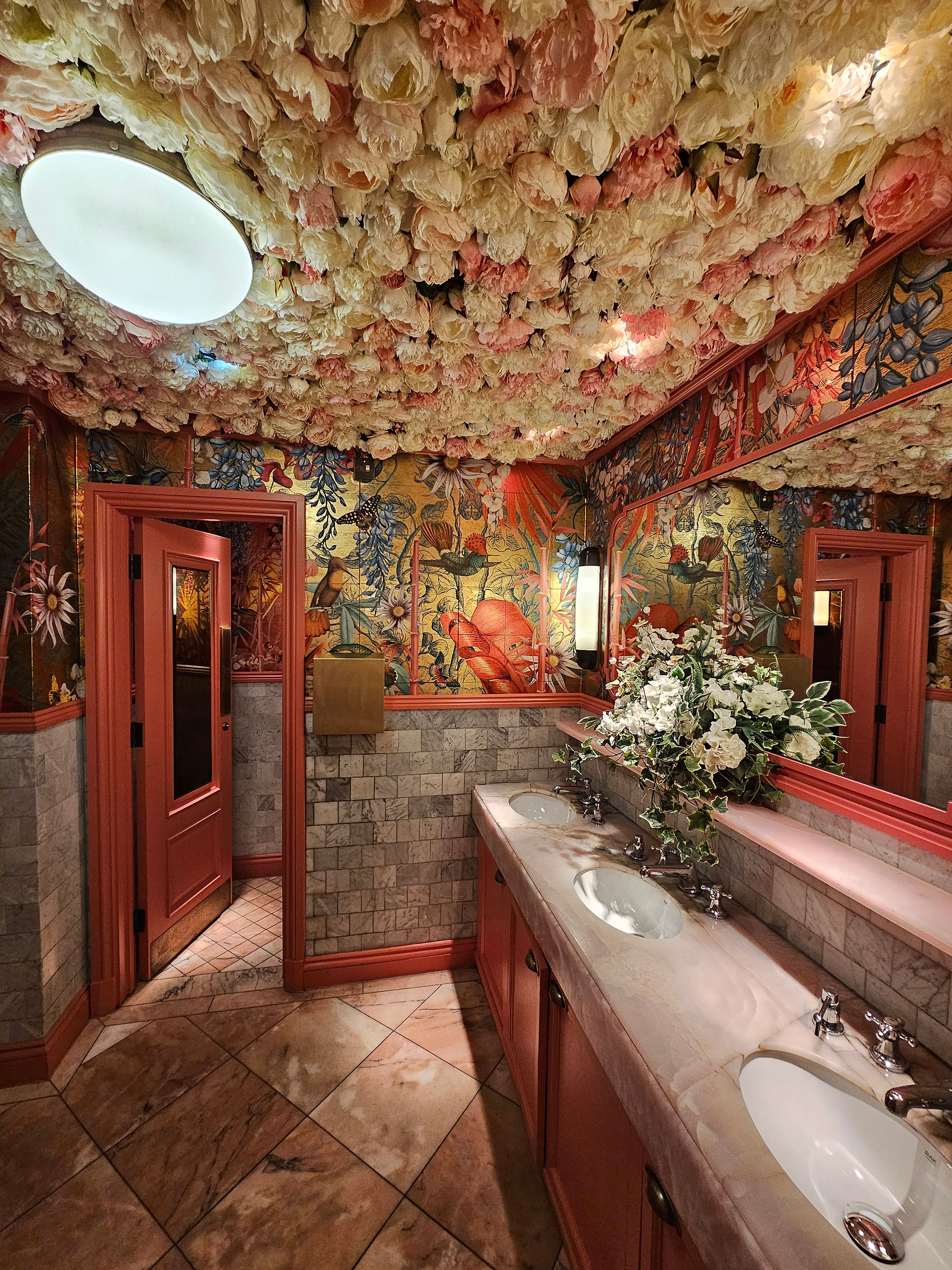 Ornate restroom at The Ivy Tower Bridge with a ceiling of faux flowers, bold floral wallpaper and marble basins