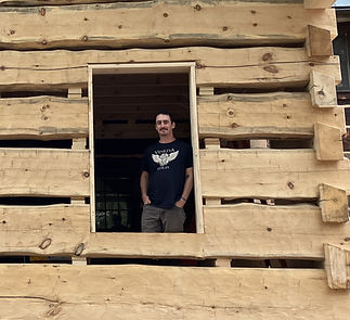 Dan Aruta in the window of a log cabin.