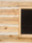 A plank jam window frame in a hand hewn log wall with masonry chinking.