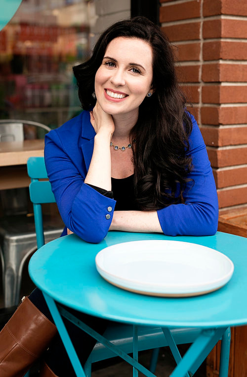 image of lauren a white brunette sitting at a cute blue cafe table, smiling