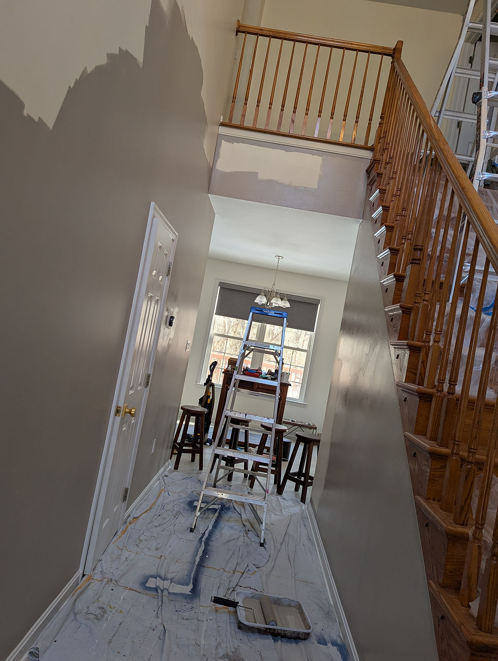 Hallway under renovation, walls partially painted gray. A ladder and stools are in the room, with drop cloths covering the floor.