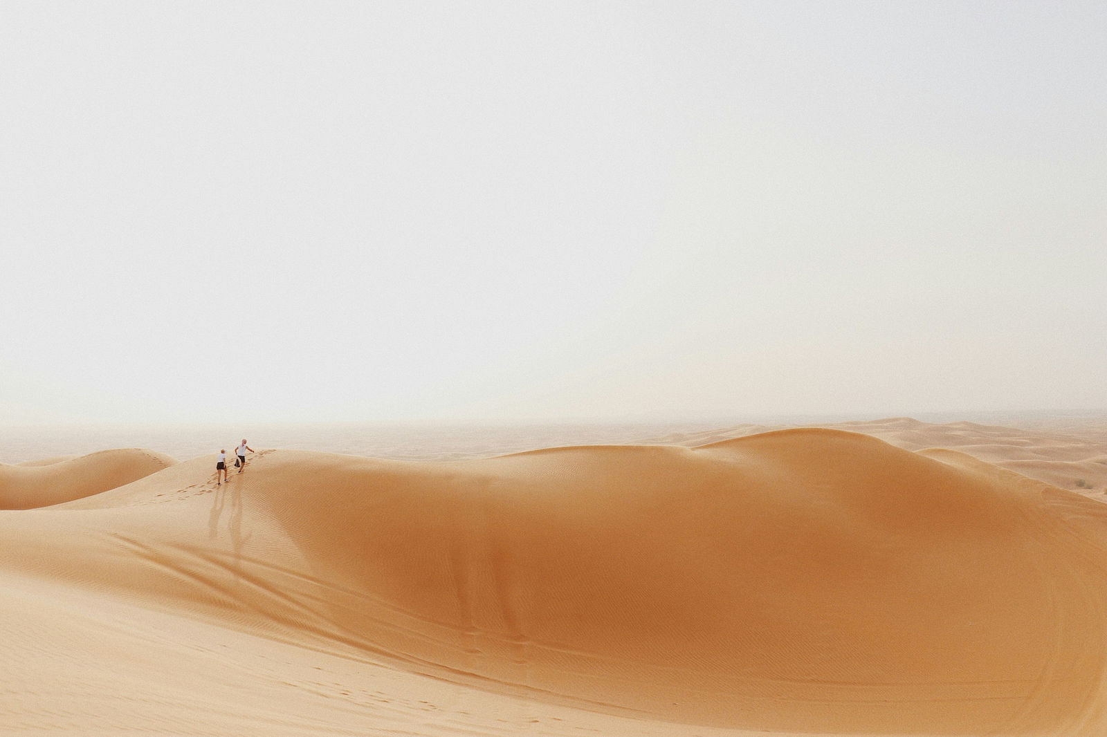 Two people walking across a vast sand dune in the Dubai desert