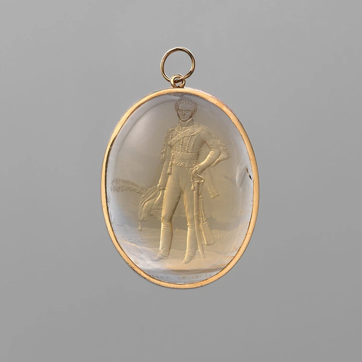 The pale yellow, oval citrine is cut as a cabochon (curved at the front and flat at the back) and highly polished. Into the back Giovanni Beltrami engraved a miniature version of Robert Lefèvre’s oil portrait of Luigi Sommariva (Galleria d’Arte Moderna, Milan). The image and its accompanying inscription are carved in reverse so that they are oriented correctly when the citrine is viewed from the front. The translucent stone’s convex shape acts like a lens to enlarge the scene and to amplify the sense of form and spatial recession. The deeply carved figure of Luigi has the startling three-dimensionality of a hologram while the shallowly carved landscape appears to expand into the far distance behind him. Beltrami convincingly rendered different materials and textures by varying the grinding strokes in the predominantly matte engraving. He highly polished discrete areas to evoke the luminous effects of sun-filled sky and bright light striking the sitter’s face. The gemstone was commissioned by the Luigi Sommariva’s father, Count Giovanni Battista Sommariva (1760–1826).