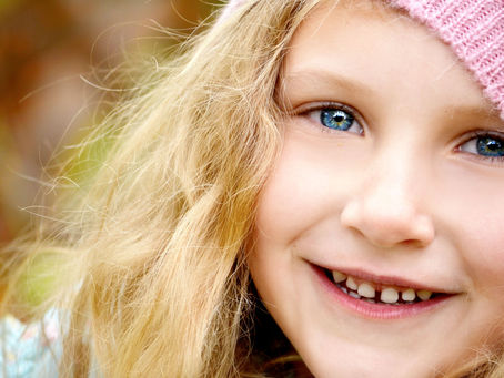 Enfant blonde souriante avec bonnet rose, yeux bleus pétillants. Atmosphère lumineuse et joyeuse, fond flou automnal. Photo pour illustrer le programme en ligne Alphazen pour réguler le nerf vague et apaiser le stress et l'anxiété