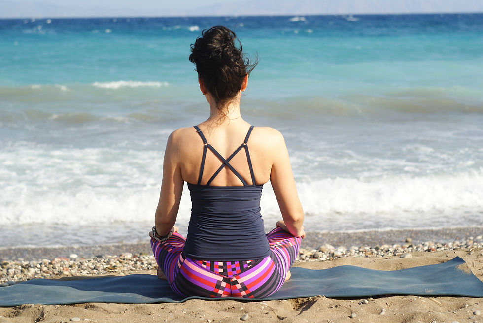 Femme assise en méditation sur une plage, portant un débardeur noir et un legging coloré. Mer turquoise en arrière-plan. Atmosphère sereine. Pour l'illustrer l'effet de l'inspiration et de l'expiration sur le nerf vague en vue de ralentir votre coeur instantanément grâce à la théorie polyvagale