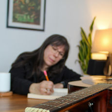Jan writing in her notebook with her guitar in front of her.