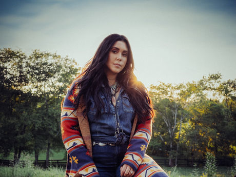 Jenna LaMaster poses at sunset in a denim outfit and patterned coat, holding a lasso in a grassy field.