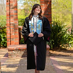 Girl standing with her graduation gown, smiling and holding her graduation cap.