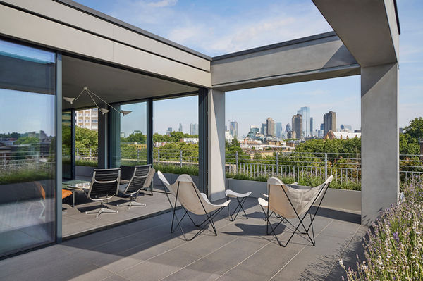 Looking through the open-plan living space and pergola-framed terrace at Clerkenwell Rooftop towards the City of London skyline, with full-height sliding glazing stacked to the sides.
