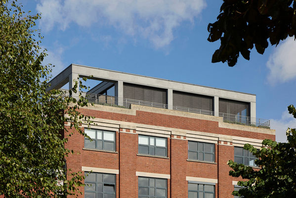 Closer view of Clerkenwell Rooftop from the park through trees, with the external shading shutters lowered across the full-height glazing.