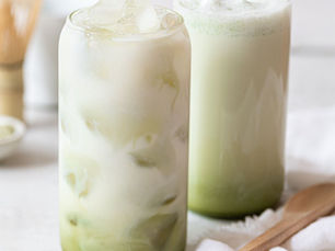 Iced Matcha Latte und heißer Matcha Latte in zwei hohen Gläsern mit japanischem Chasen und Bambuslöffel