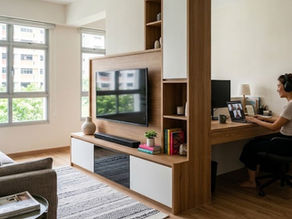 Cosmos Decor Singapore 4-room BTO renovation feature: A creative carpentry room divider creates a distinct Work-From-Home (WFH) nook without closing off the open-concept living area. The custom oak unit houses a TV console on one side and a desk on the other, demonstrating multi-functional storage science for compact HDB flats. Iconic Singapore residential blocks are visible outside.