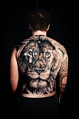 Tatuaggio sulla schiena intera che ritrae un leone fiero e maestoso, con una croce in negativo su un occhio, realizzato da Cindy Tattoo e fotografato da ID Communication Srl