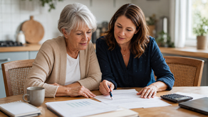 Older woman and adult daughter reviewing estate planning documents together at a kitchen table, with a calculator, notebook, and laptop nearby.