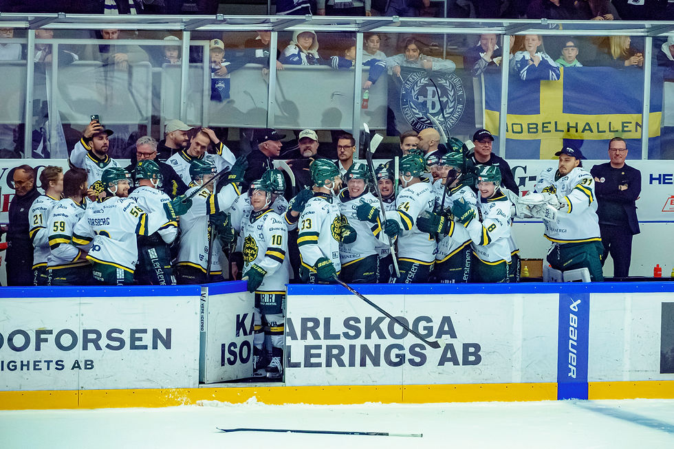 Hockey players in white jerseys celebrate on the bench. Audience with flags watch behind glass. Mood is jubilant. Text: "Nobelhallen."
