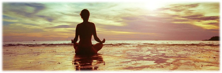 A lady sitting on the beach meditating.