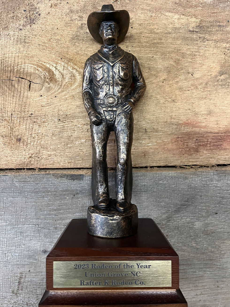 Bronze cowboy trophy, "Rodeo of the Year 2023" plaque, wooden background.