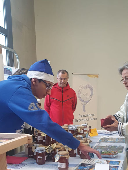 Enzo montrant aux clients des produits sur le stand Espérance bleue au marché de Noël
