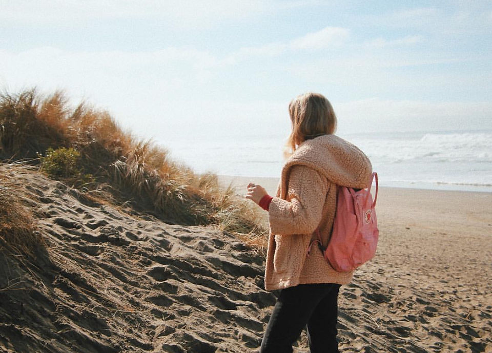 A girl standing alone at the beach with a backpack