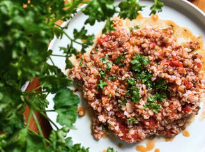 A deep ceramic bowl filled with vibrant buckwheat risotto, simmered in tomato sauce and glistening with olive oil. Garnished with chopped herbs and a rustic spoon to the side, it’s comfort food rooted in tradition and sustainability.