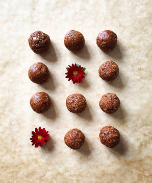 Twelve round energy balls made with dates and nuts, neatly arranged in a grid on parchment paper with two red edible flowers.