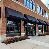 Street-level view of a commercial brick building with black awnings and large windows, suitable for retail storefront renovations in London, Ontario.