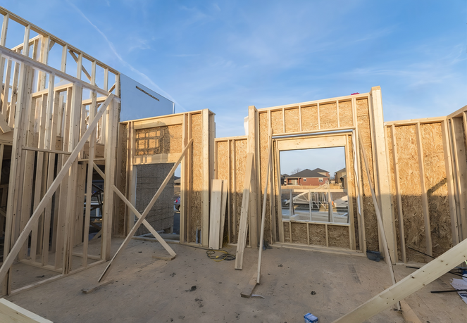 Framing and plywood sheathing in progress for a residential home addition under a clear blue sky.
