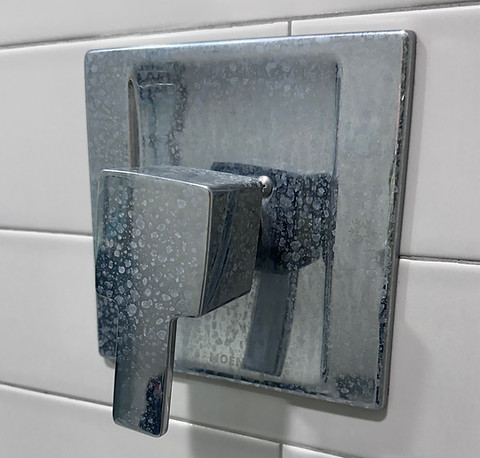 Chrome shower fixture with visible water spots and mineral buildup before cleaning